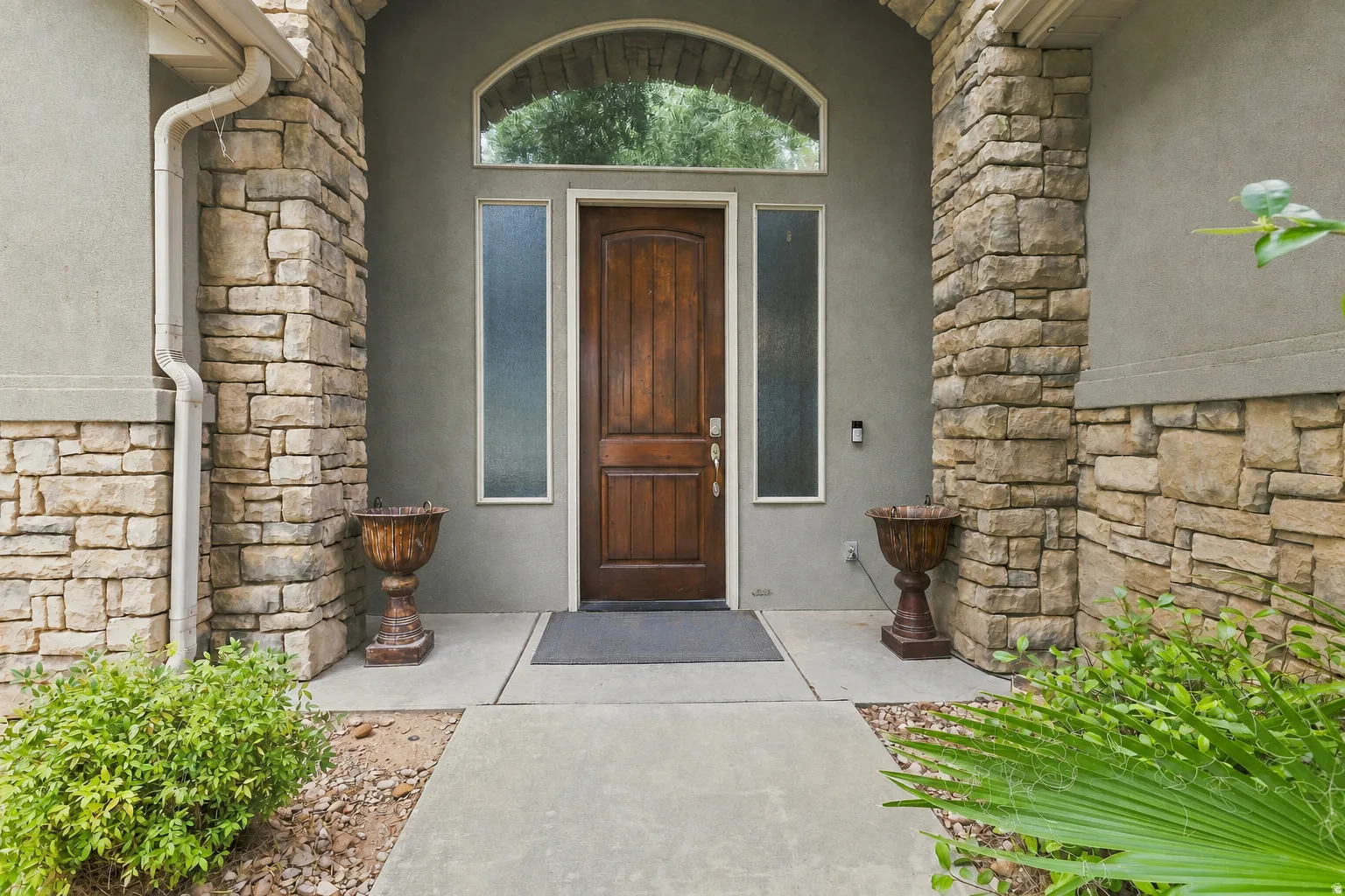 Arched entryway featuring a paneled wood door, transom window, and stacked stone accents