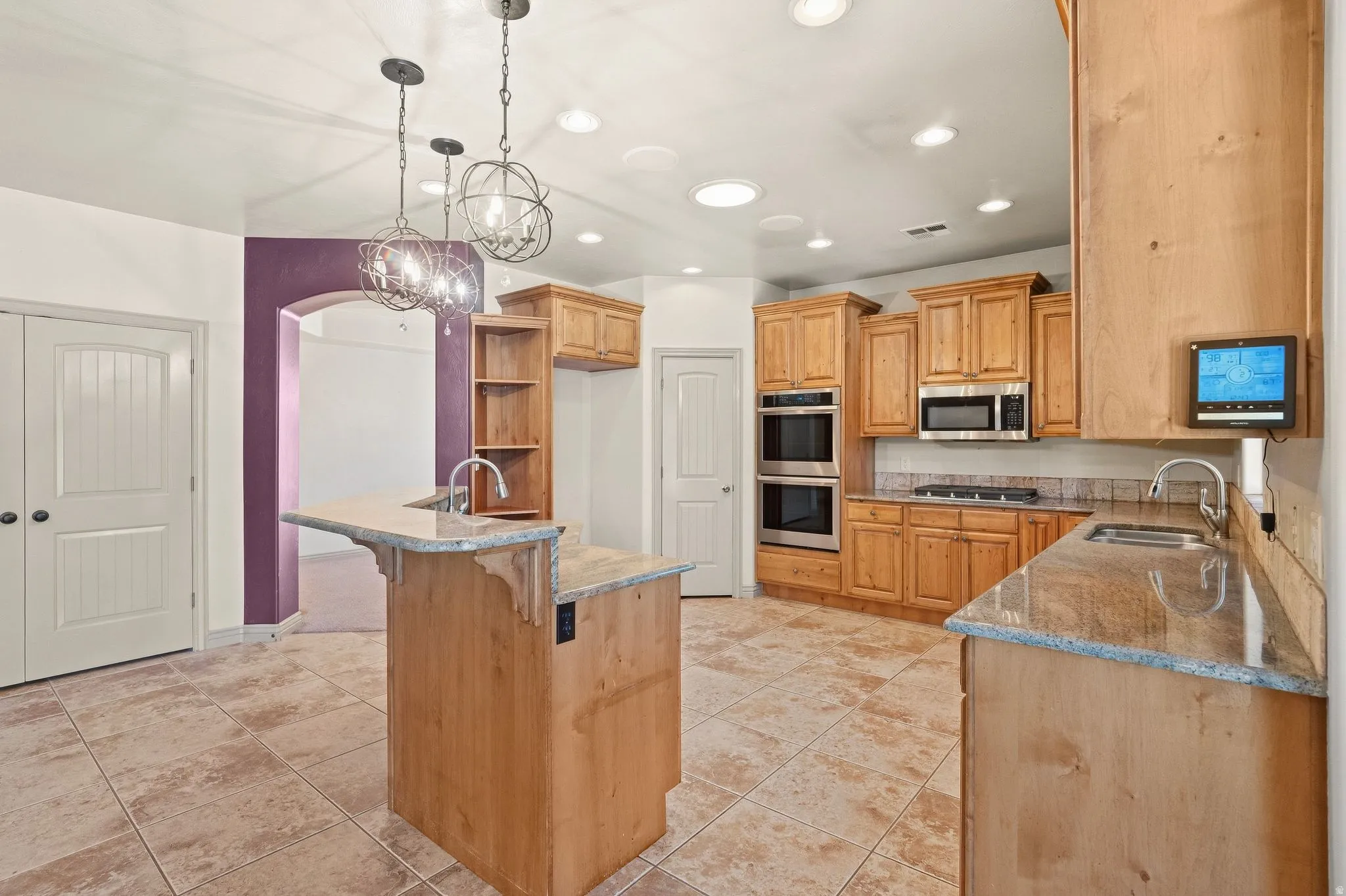 Spacious kitchen featuring light wood cabinetry, stone countertops, double wall ovens, a built-in microwave, and tile flooring