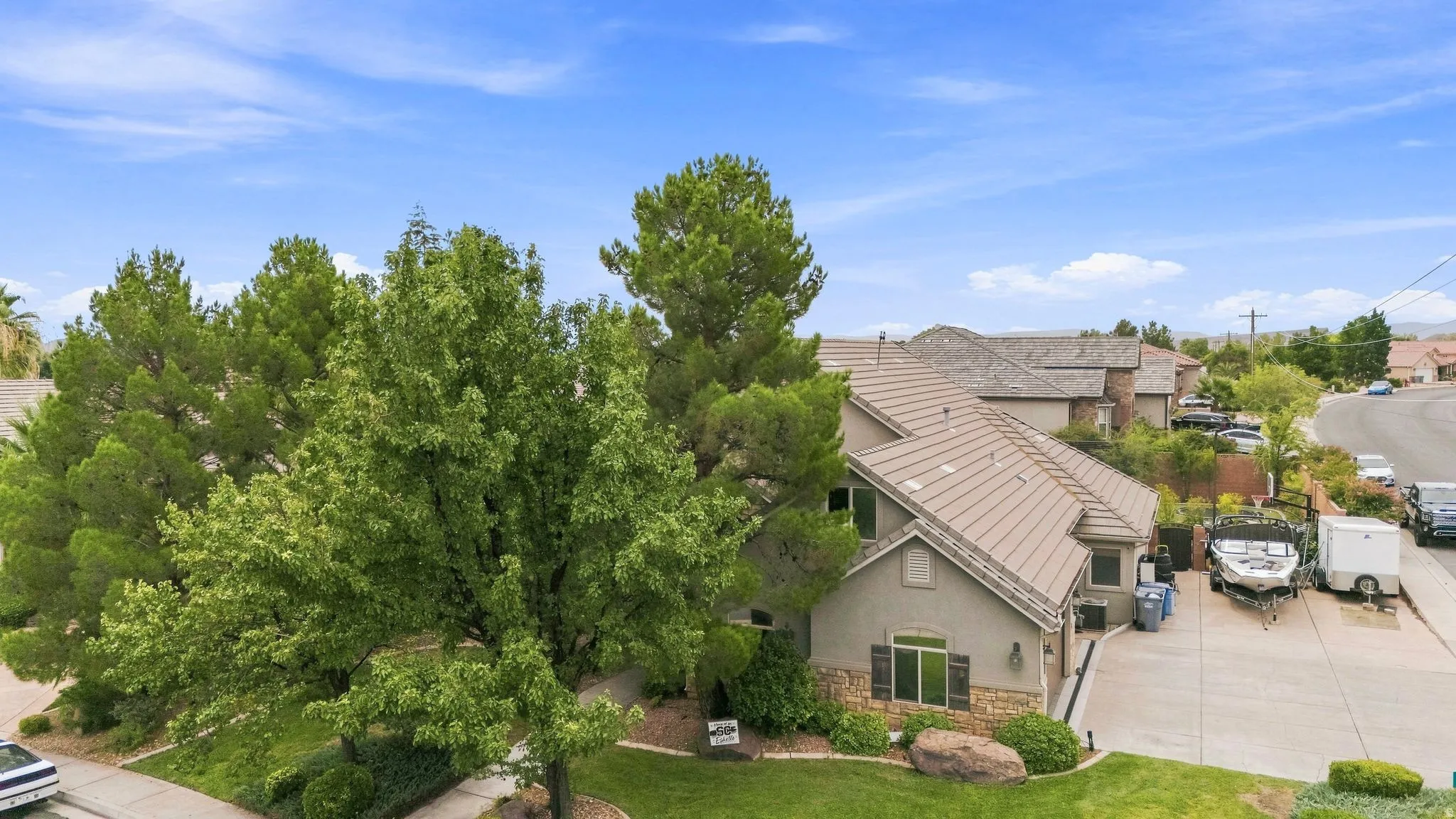 Stucco exterior with stone accents, mature trees, and a tile roof