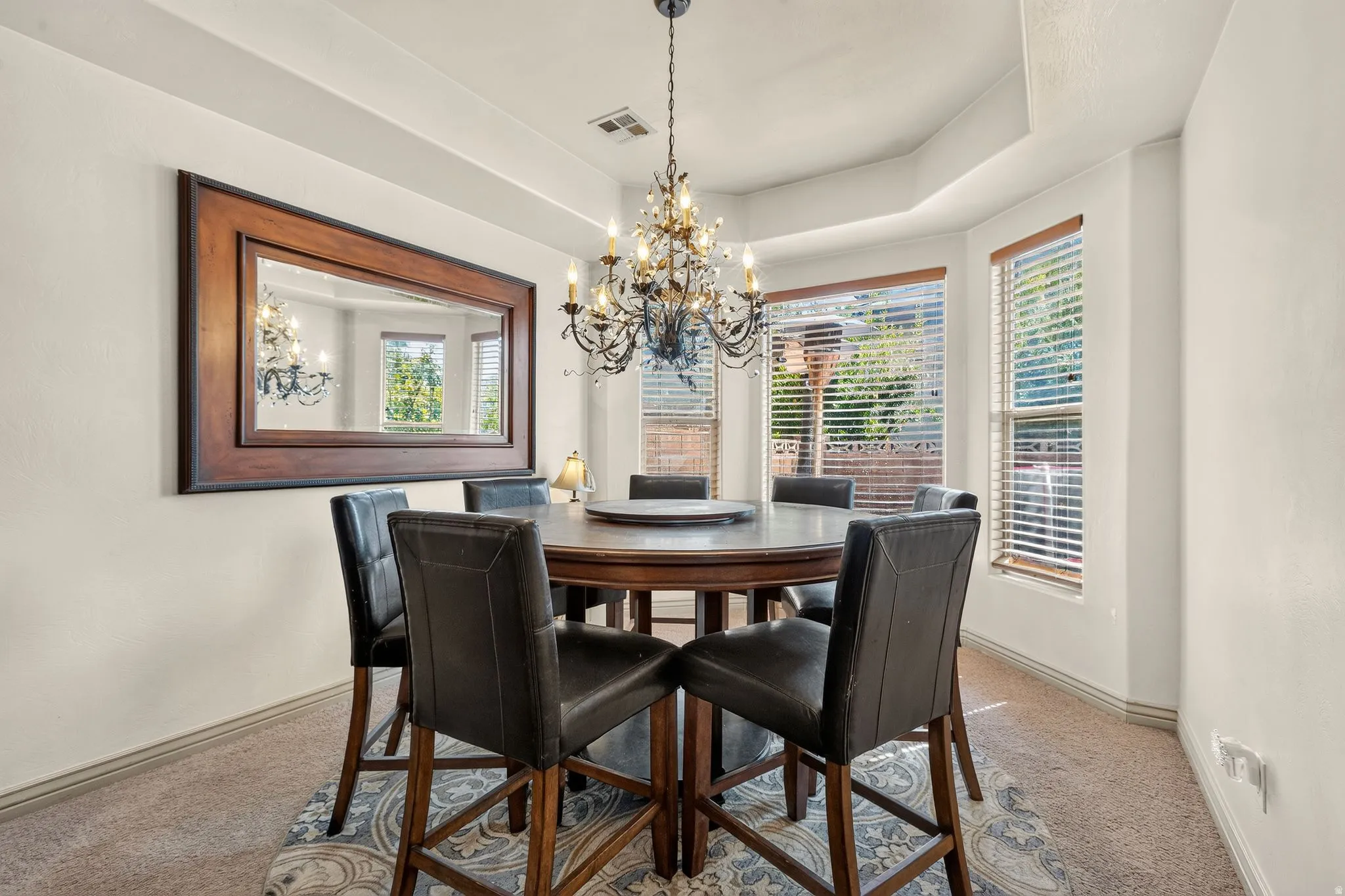 Bay window with multiple panels, chandelier lighting fixture, wall-mounted mirror with wood frame, and neutral wall tones