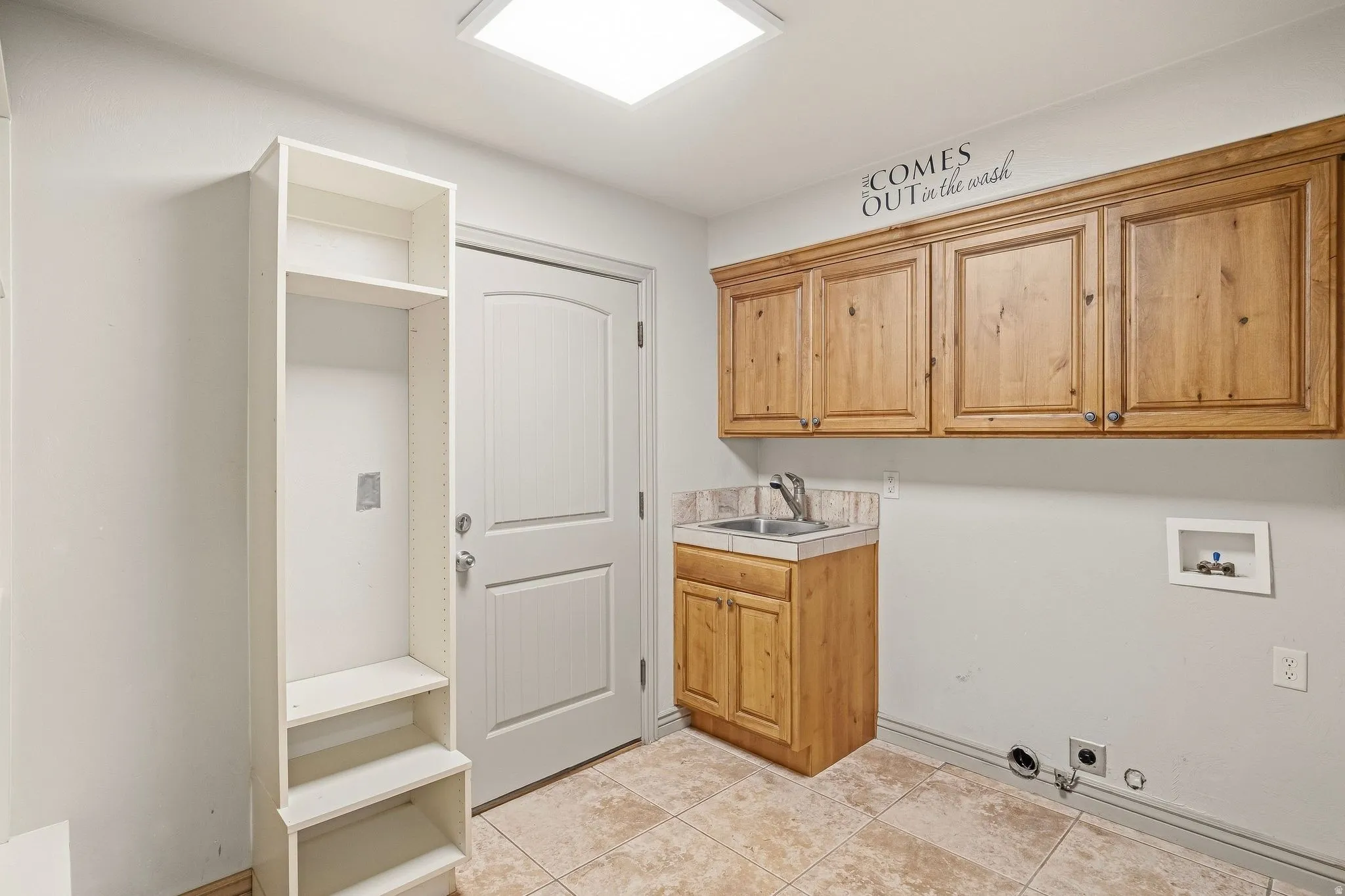 Utility room with built-in wood cabinetry, a utility sink, and tile flooring