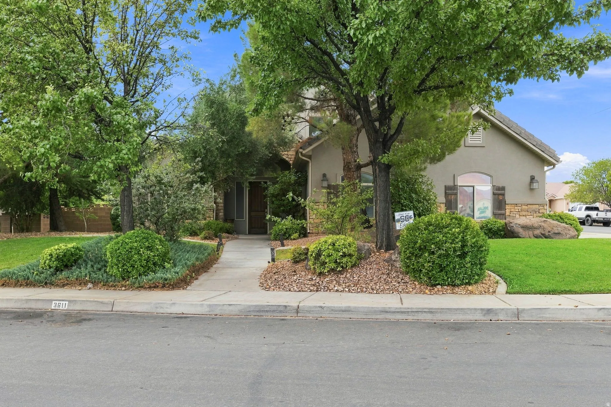 Stucco exterior with stone accents, mature trees, manicured shrubs, and a concrete walkway