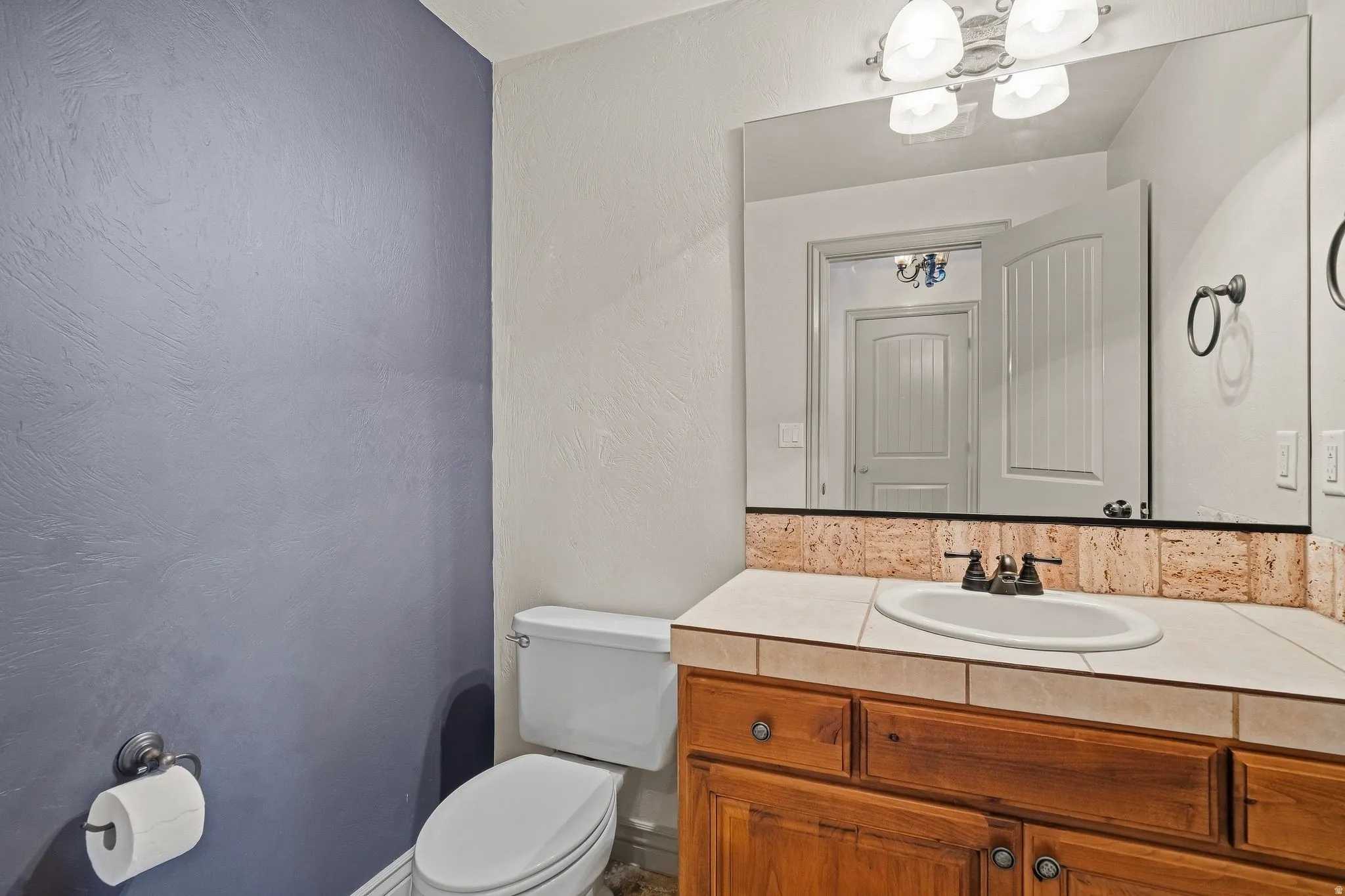 Vanity with wood-finish cabinetry, tile countertop, and a white oval sink