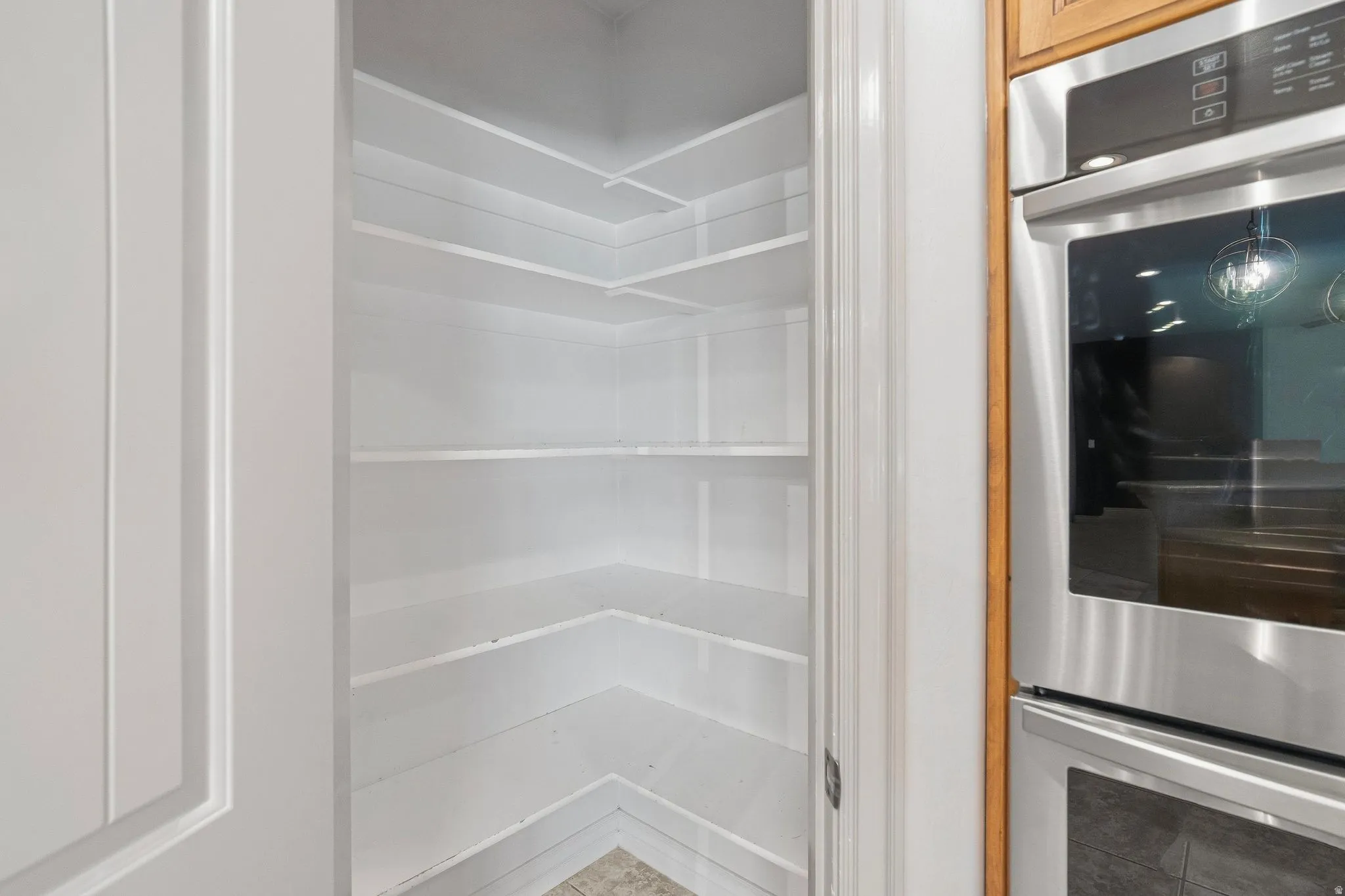 Walk-in pantry with extensive shelving, paneled door, and adjacent built-in stainless steel double ovens