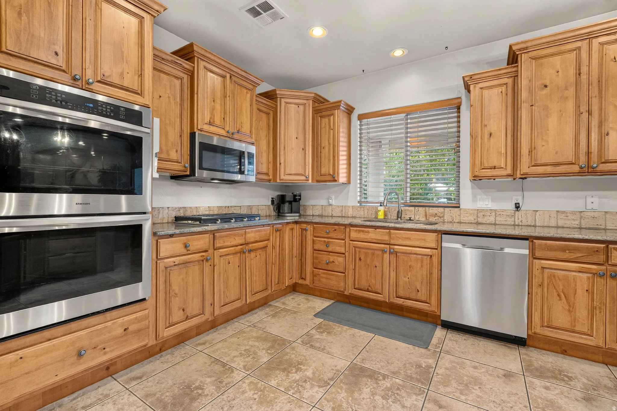 Kitchen featuring wood-finish cabinetry, stainless steel double wall ovens, a coordinating stainless steel dishwasher, a built-in microwave, and tile flooring