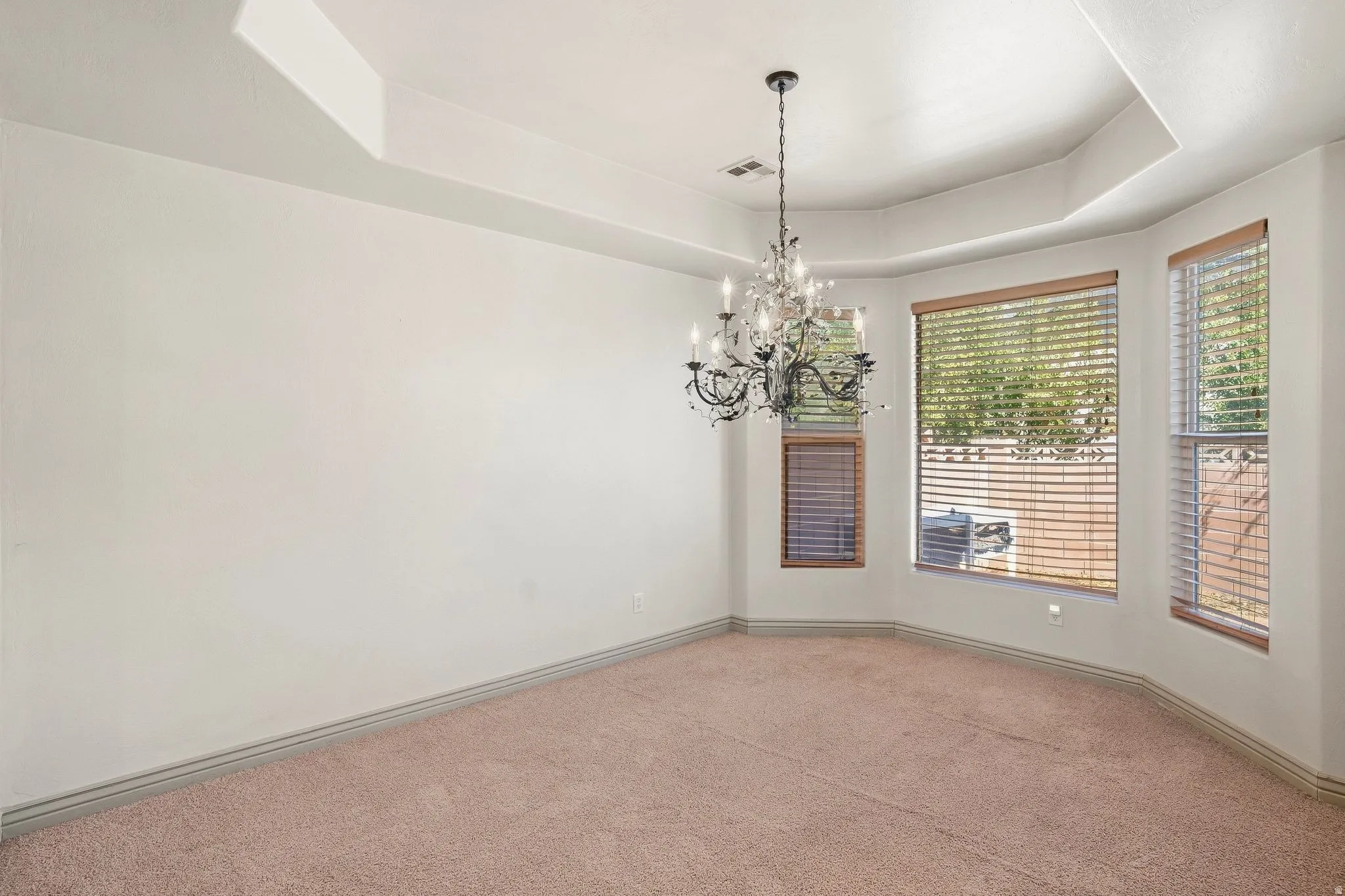 Tray ceiling with a decorative chandelier and multiple windows with wood-tone blinds