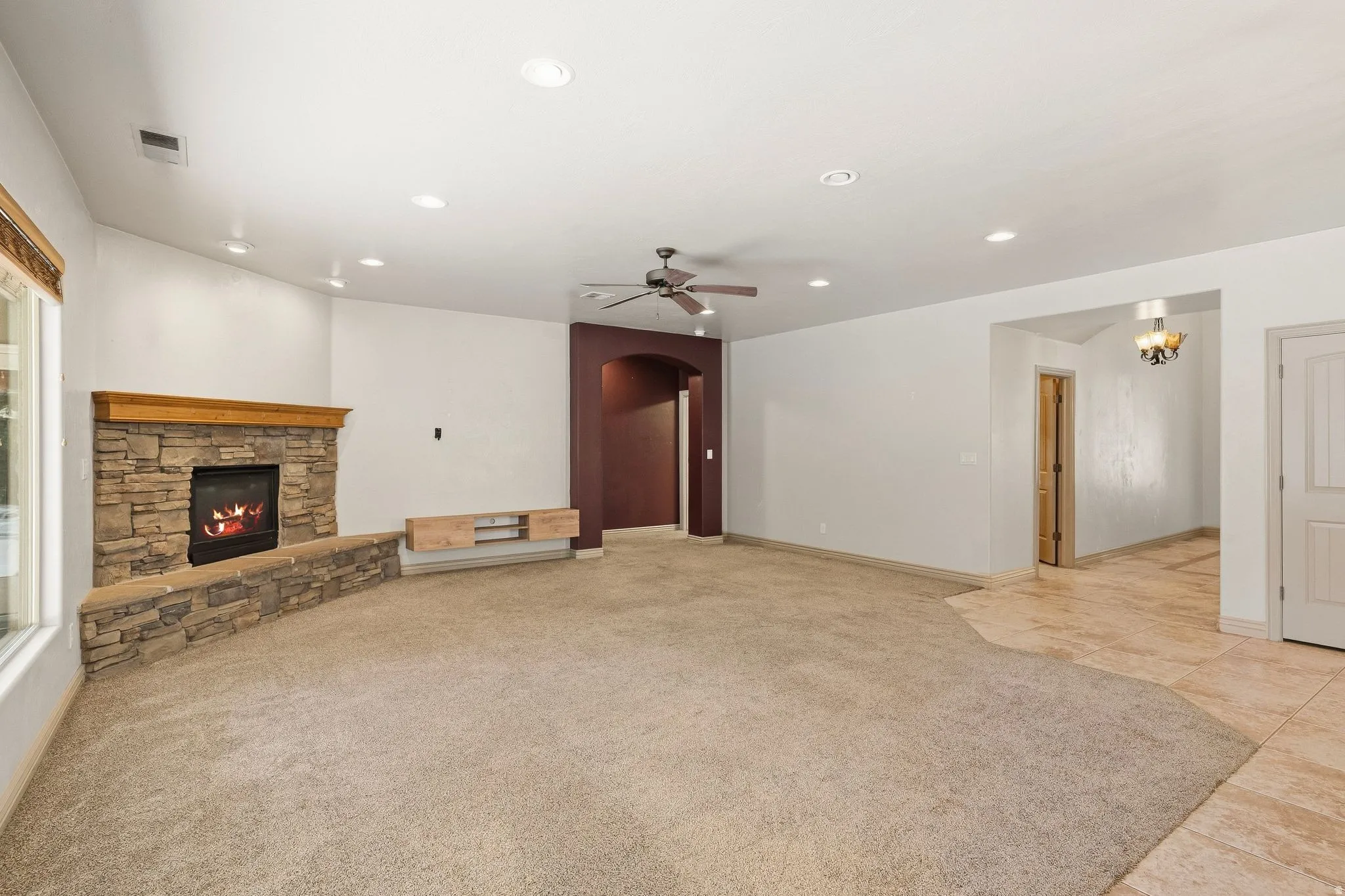 Carpeted living area featuring a stone-clad fireplace with a wood mantel, recessed lighting, and a ceiling fan