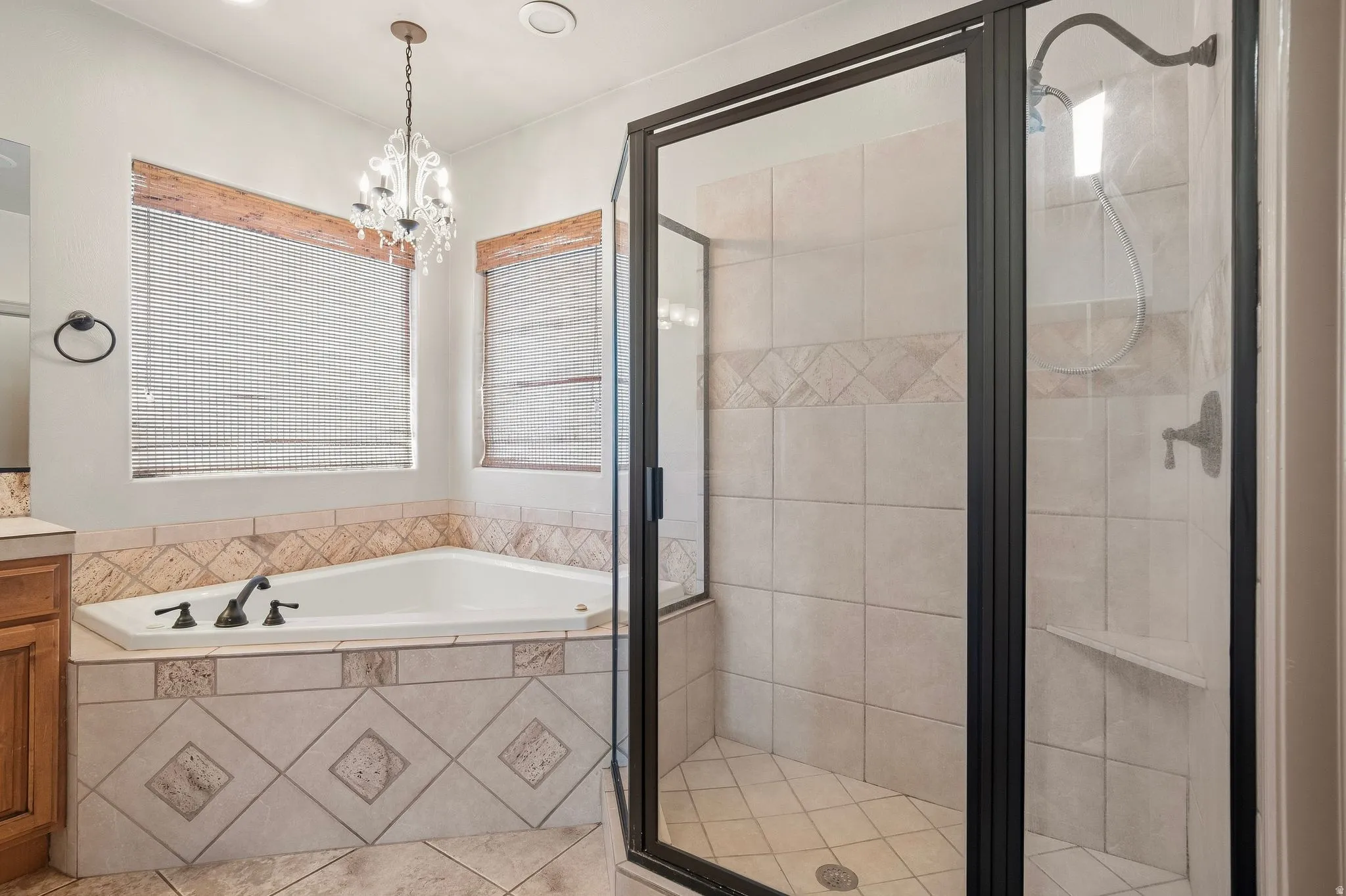Built-in corner bathtub, tiled shower enclosure with glass door, chandelier lighting fixture, and window treatments