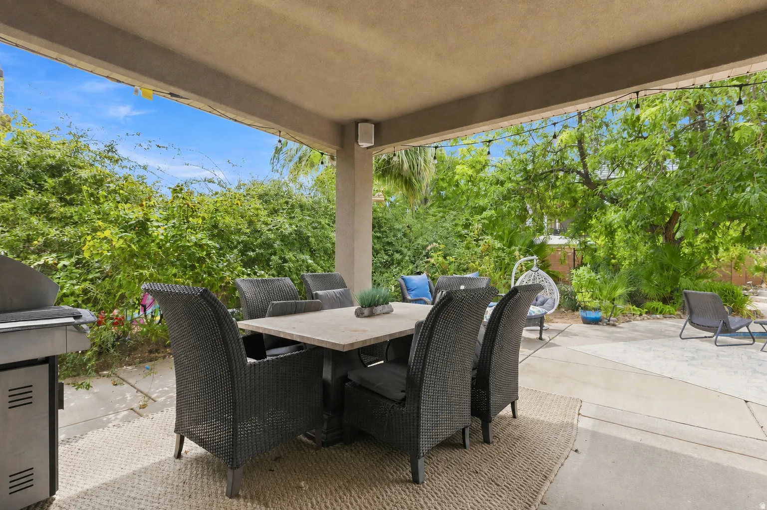 Covered patio featuring string lighting, integrated outdoor speakers, and mature landscaping