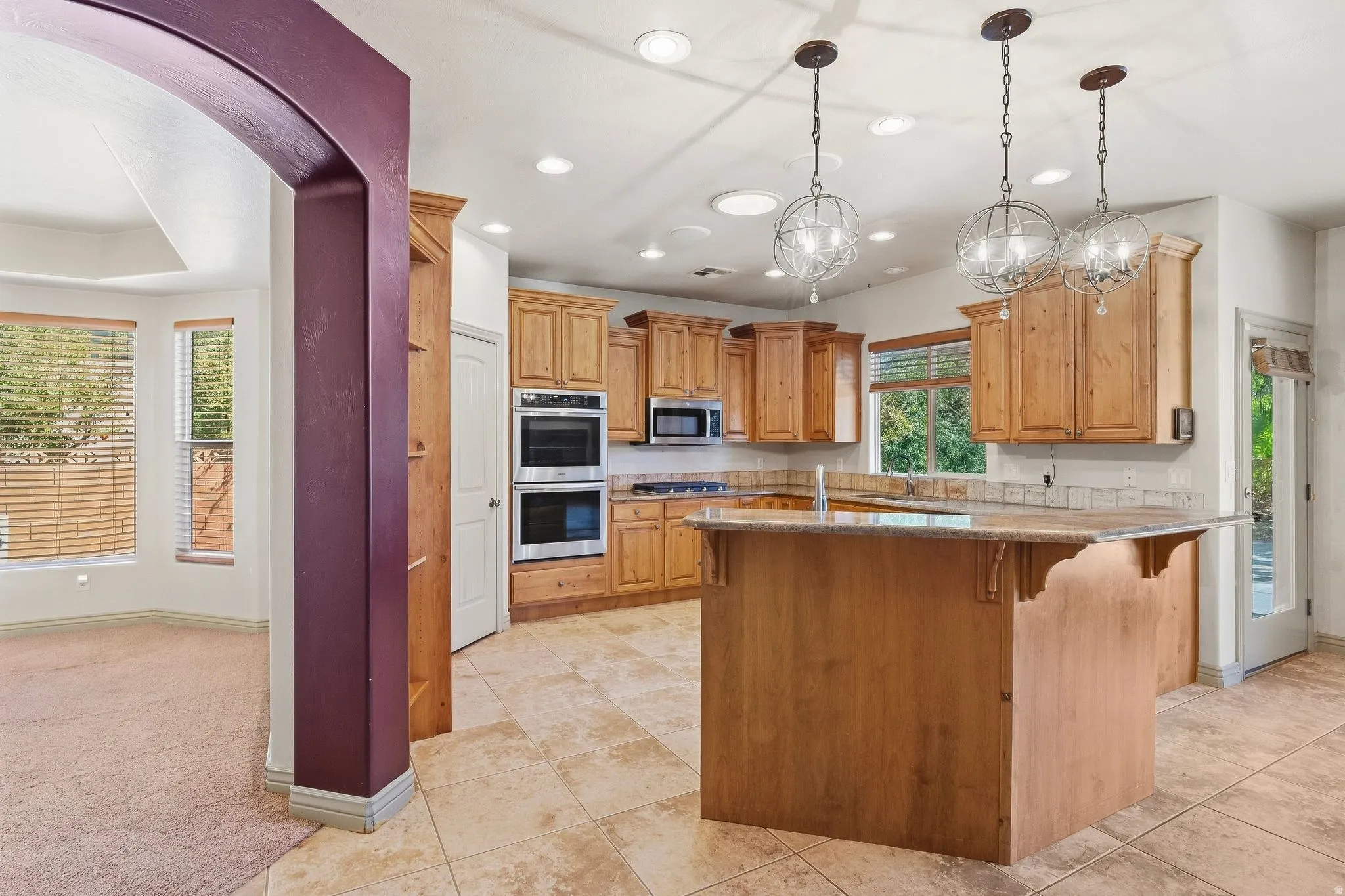 Kitchen featuring light wood cabinetry, stone countertops, stainless steel double ovens, an island with seating, and recessed lighting