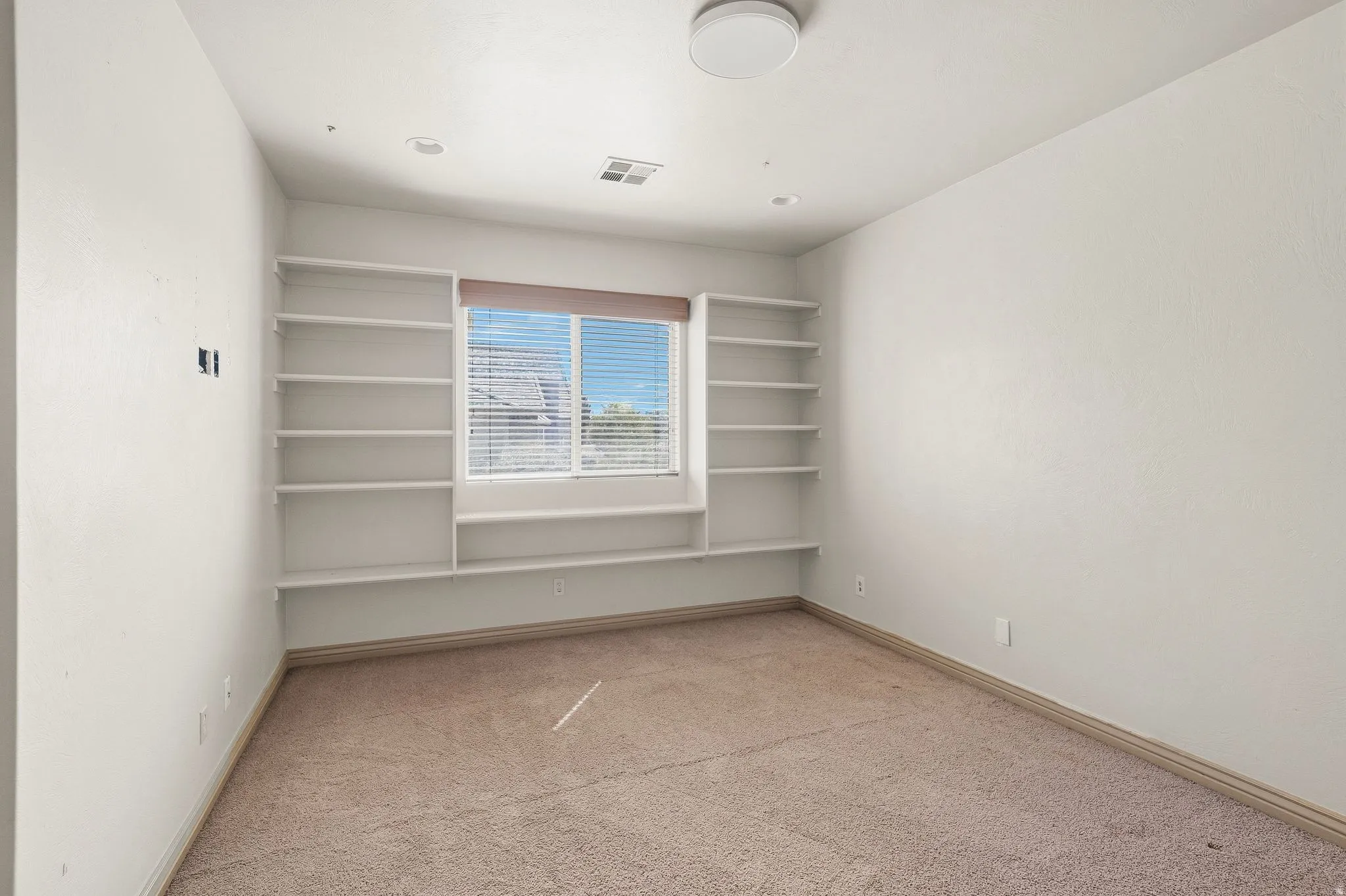Built-in shelving flanking a window, overhead flush-mount lighting, and recessed ceiling lights