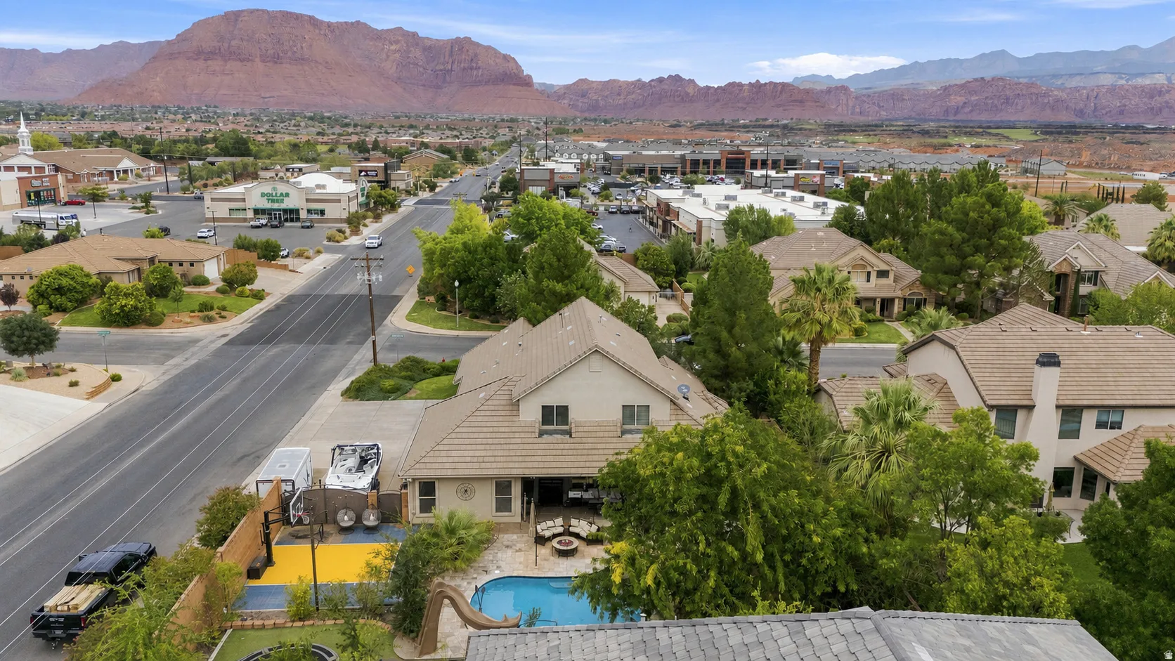 Property with a private pool, outdoor patio, and mature trees, surrounded by residential and commercial structures with mountain scenery in the background
