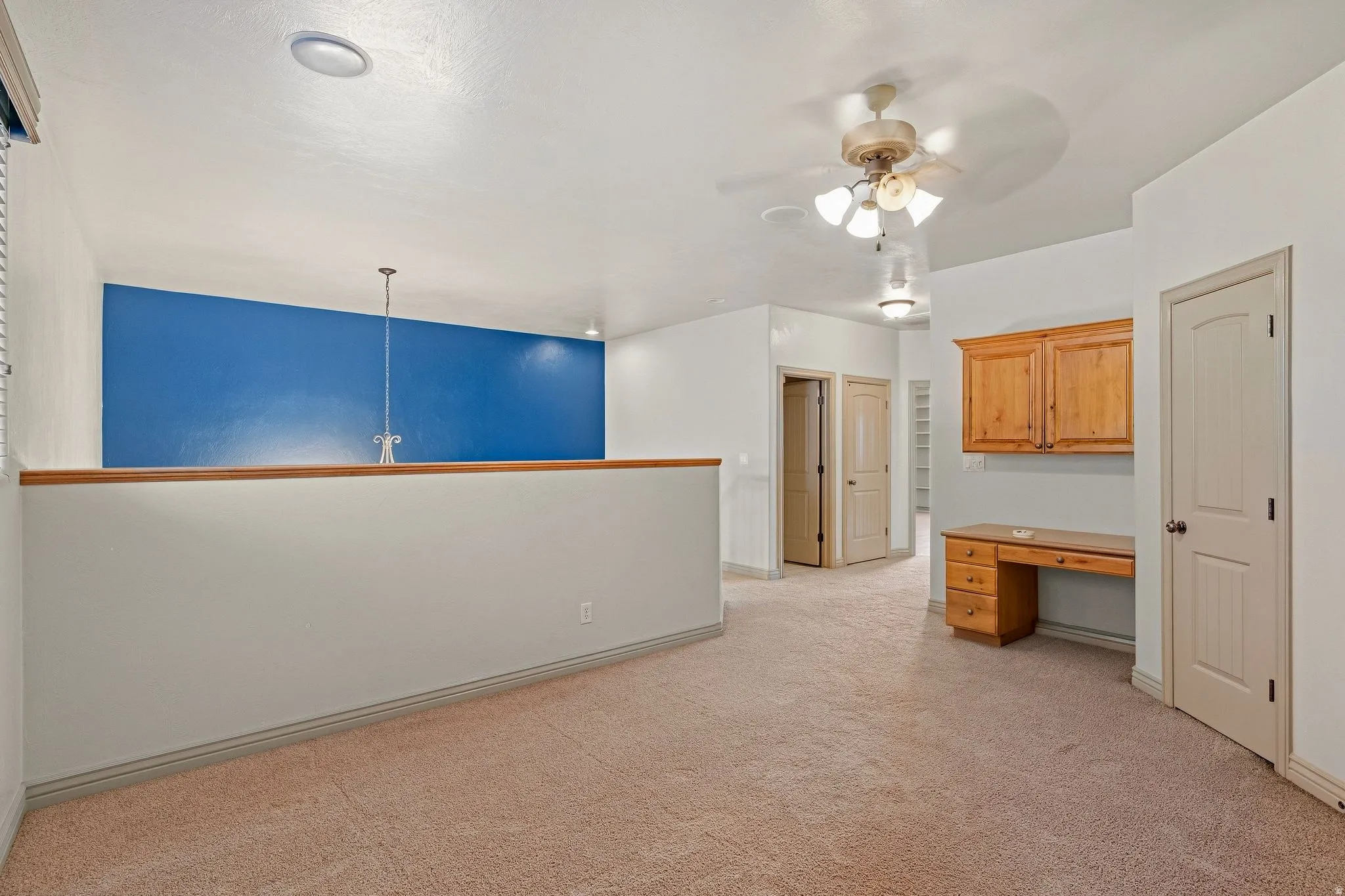 Carpeted loft area featuring a built-in wood desk with overhead cabinetry, ceiling fan, recessed lighting, and a partial wall with wood capping