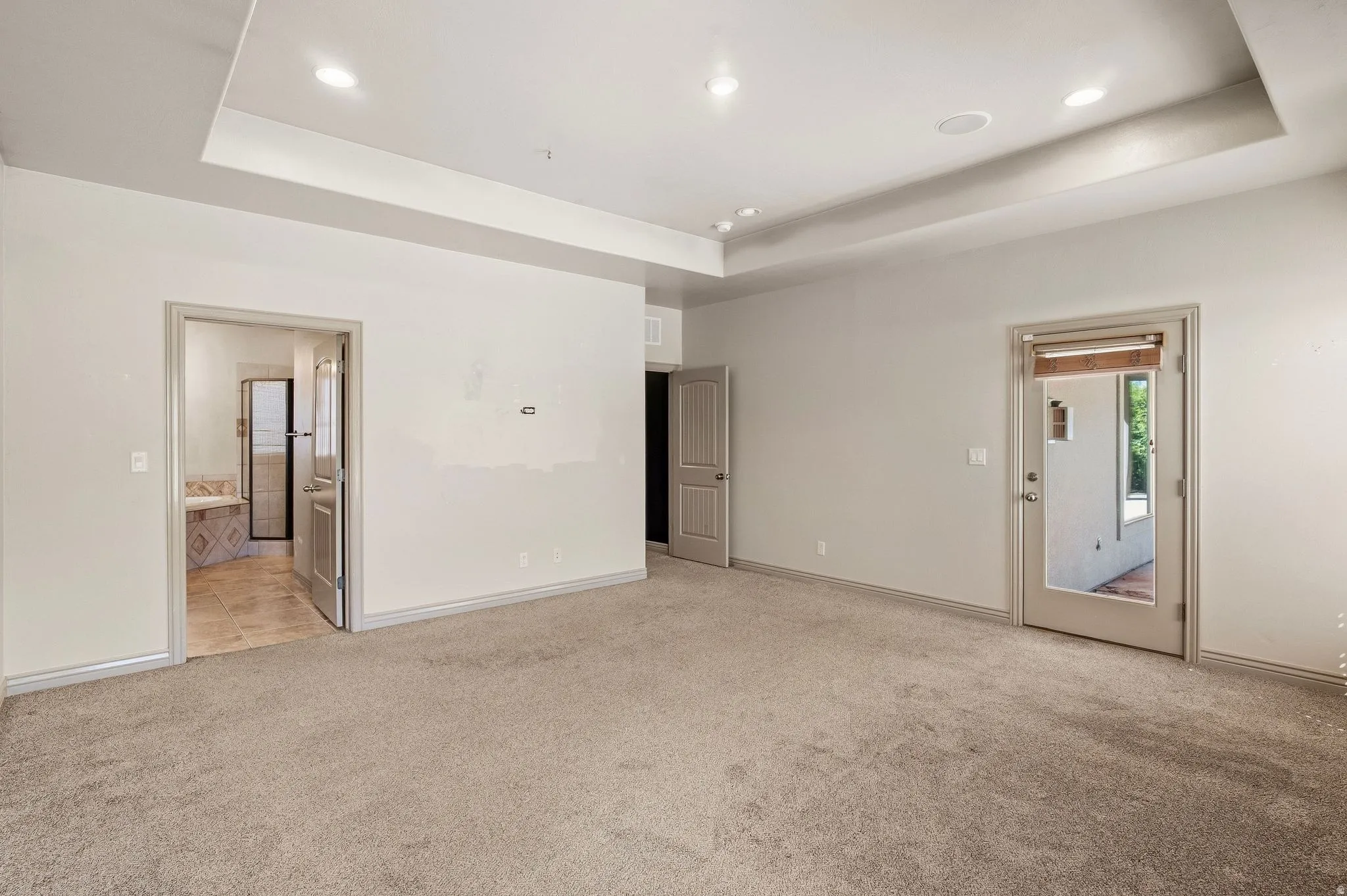 Recessed lighting, tray ceiling, full-light exterior door, and an interior doorway leading to a bathroom with a tiled floor