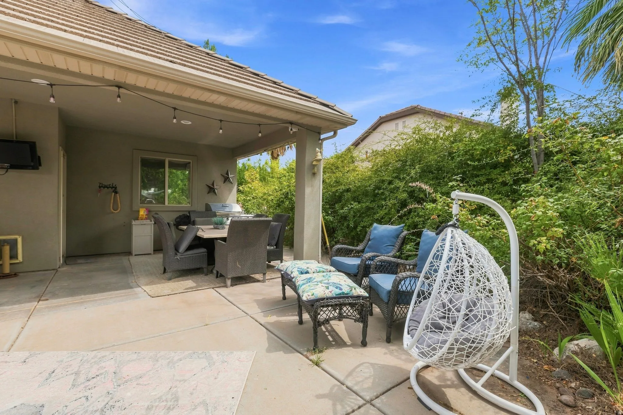 Expansive concrete patio with a covered outdoor dining area, string lighting, and mature perimeter landscaping