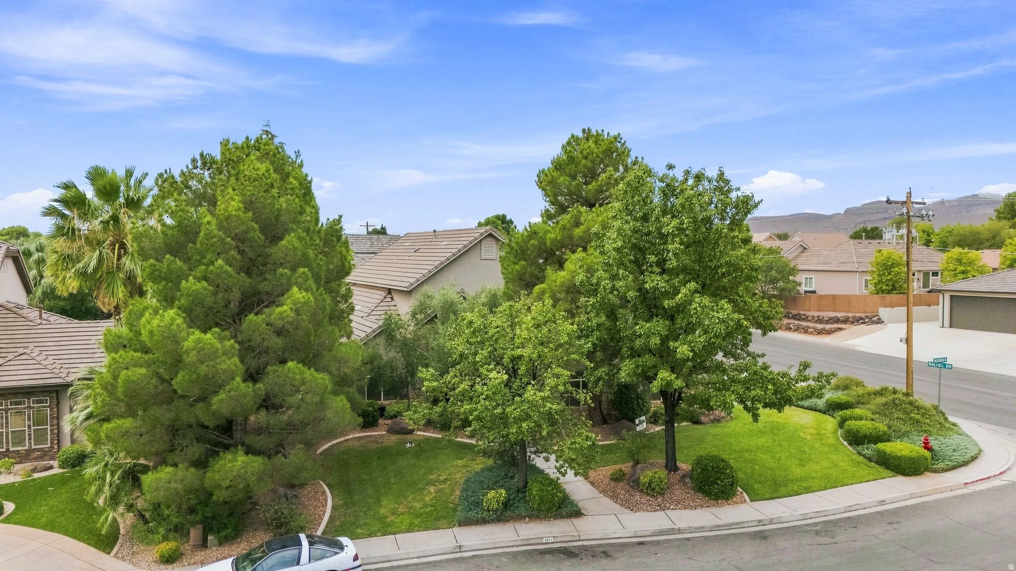 Manicured front yard with mature trees, established landscaping, and a sidewalk