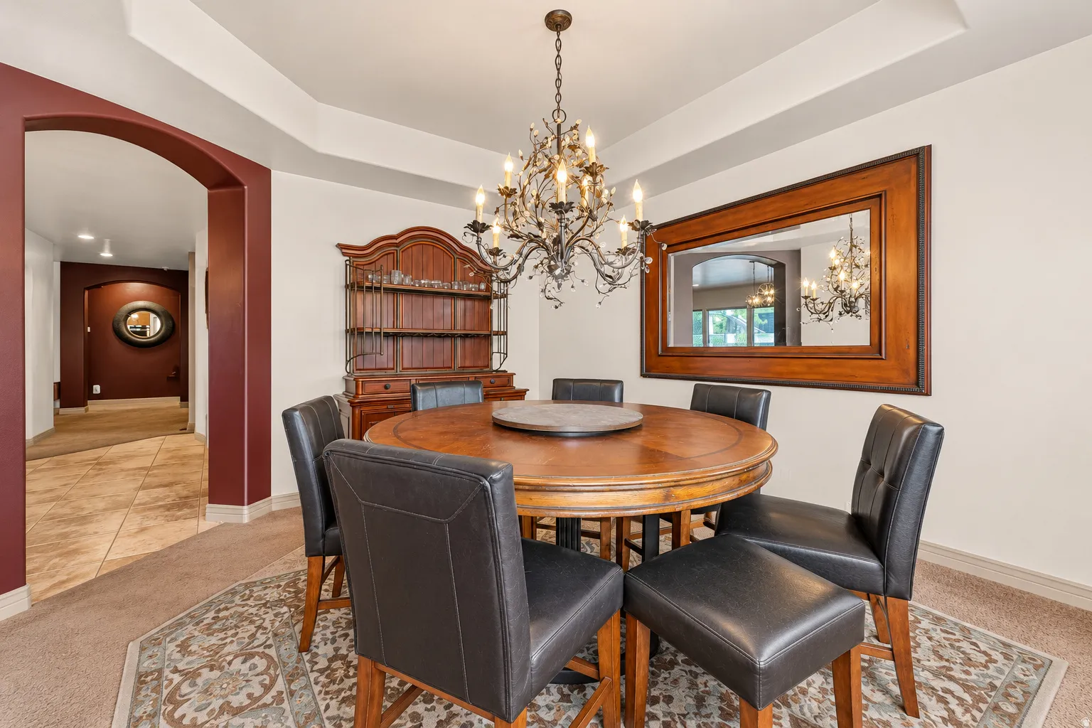 Tray ceiling detail, arched entryway, tile flooring, and wall-mounted chandelier
