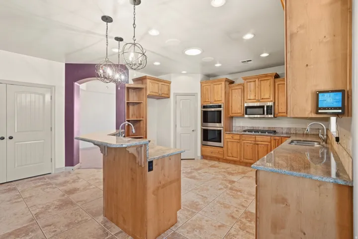 Spacious kitchen featuring light wood cabinetry, stone countertops, double wall ovens, a built-in microwave, and tile flooring
