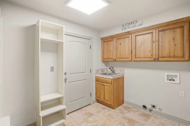 Utility room with built-in wood cabinetry, a utility sink, and tile flooring
