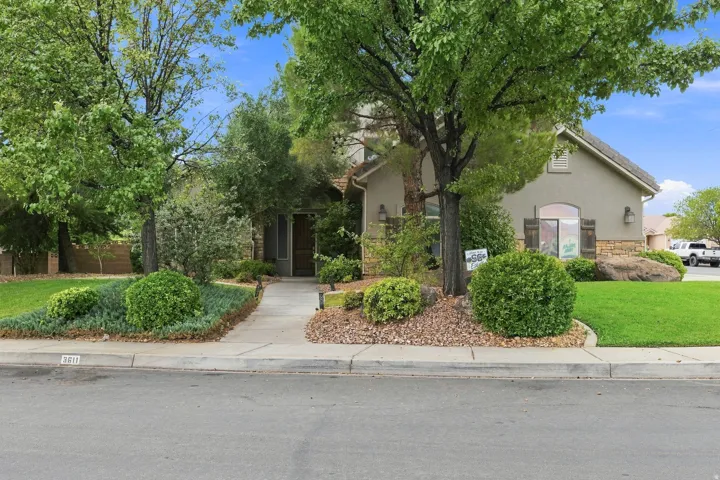Stucco exterior with stone accents, mature trees, manicured shrubs, and a concrete walkway