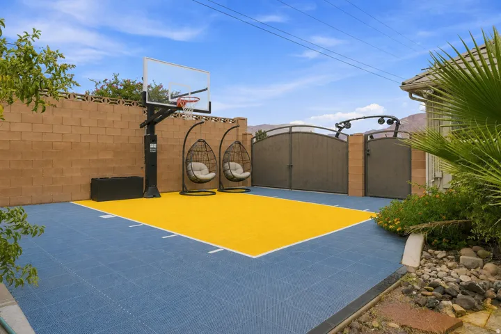Private outdoor court featuring an adjustable basketball hoop, tiled playing surface, and two hanging chairs