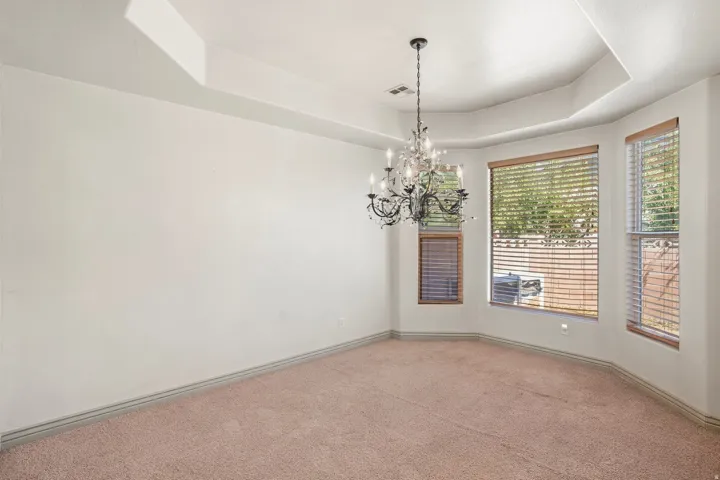 Tray ceiling with a decorative chandelier and multiple windows with wood-tone blinds