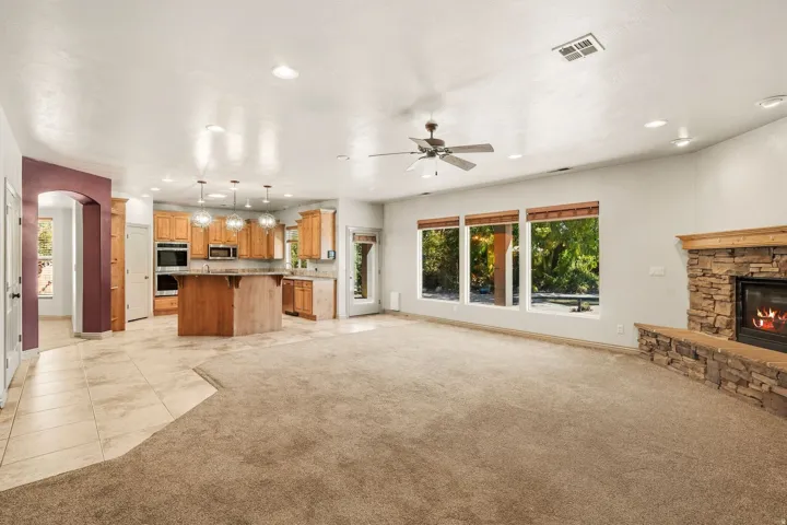 Stone-clad fireplace, recessed lighting, ceiling fan, multiple large windows, and a kitchen with wood cabinetry