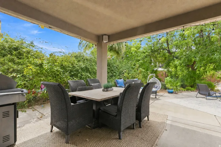 Covered patio featuring string lighting, integrated outdoor speakers, and mature landscaping