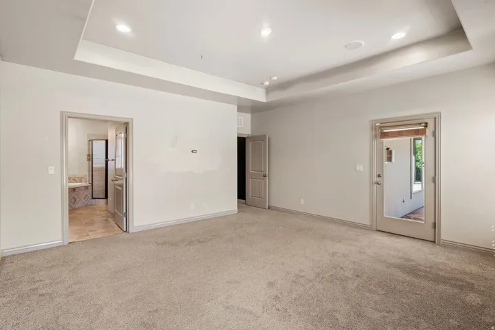 Recessed lighting, tray ceiling, full-light exterior door, and an interior doorway leading to a bathroom with a tiled floor