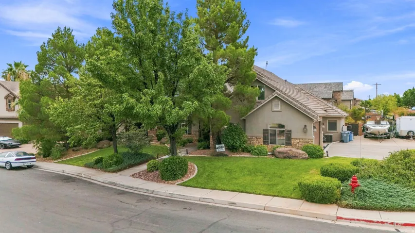 Stucco exterior with stone accents, mature trees, manicured lawn, and a paved driveway