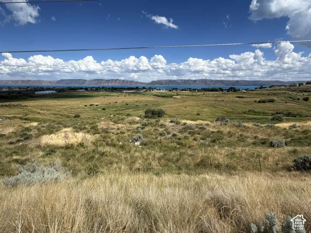 Expansive land parcel featuring natural grasses and distant water body with mountainous backdrop