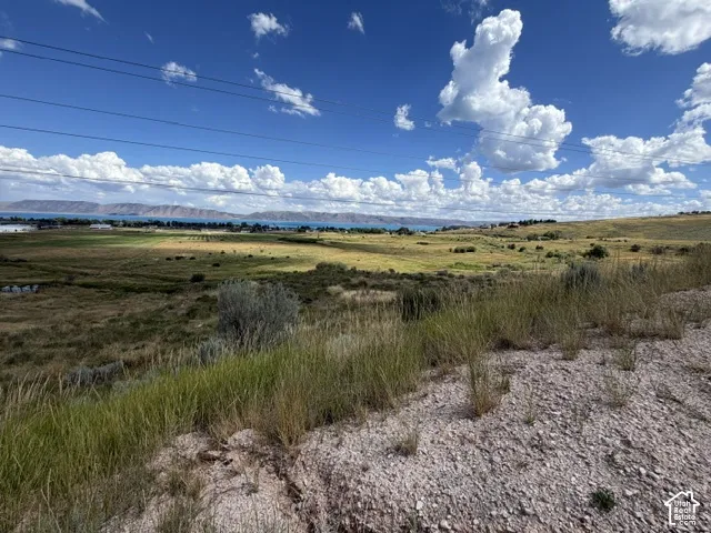 Expansive natural landscape featuring a distant body of water, rolling hills, and a clear sky with clouds