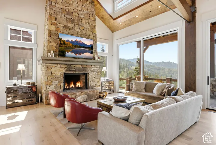 Floor-to-ceiling stone fireplace, soaring vaulted wood-finish ceilings, wood-finish flooring, large sliding glass doors, and exposed wood beams