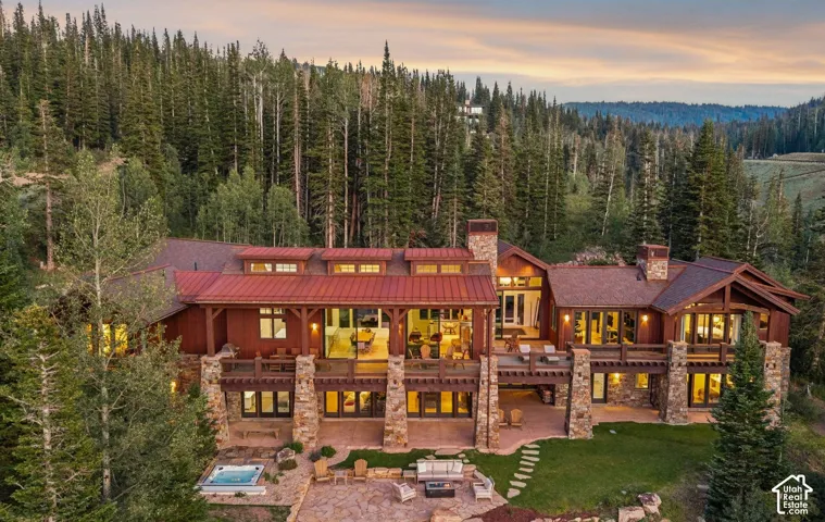 Mountain estate featuring a natural stone foundation, metal roofing, expansive wood decking, integrated stone patio, and an in-ground spa