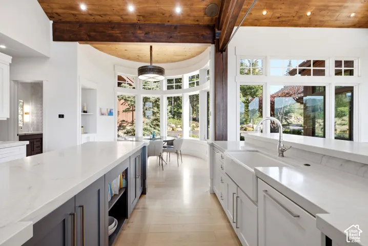 White countertops, wood-finish flooring, wood beam ceiling, white cabinetry, and large windows
