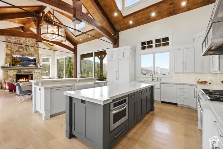 Open-concept living area with vaulted wood beam ceilings, a stone fireplace, and light wood-finish flooring