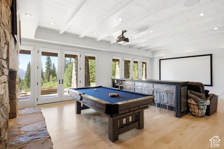 Stone fireplace, light wood-finish flooring, white beamed ceiling, built-in bar, and multiple sets of French doors