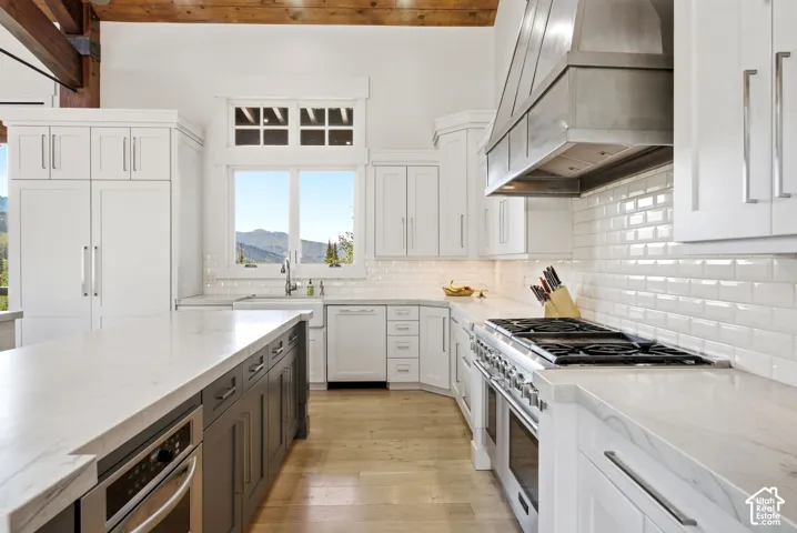 Kitchen featuring white shaker cabinetry, light wood-finish flooring, a stainless steel commercial-style range, and a large central island with a built-in microwave