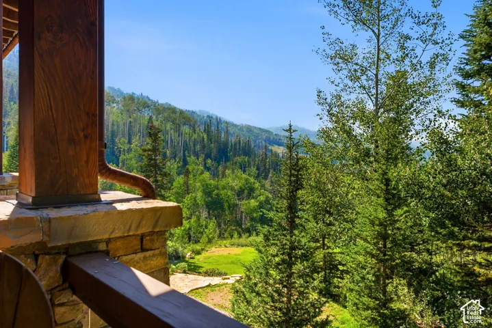 Stone patio with a wood support beam and integrated downspout, framed by mature trees and distant mountains