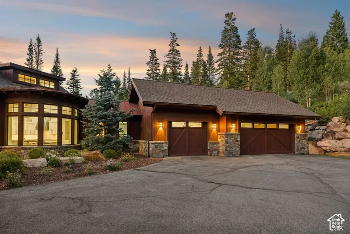 Wood-sided exterior with stone accents, featuring a two-car garage with wood doors and exterior lighting, and a prominent bay window