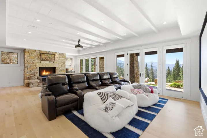 Exposed beam ceiling with recessed lighting, stone fireplace, light wood-finish flooring, multiple French doors, and a large projection screen