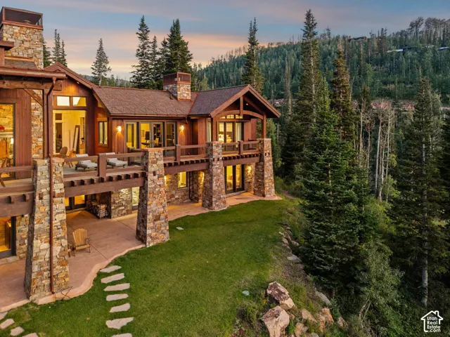 Multi-level residence featuring a stone and timber facade, multiple outdoor balconies, a lower-level patio with stone slab walkway, and a sloped lawn area