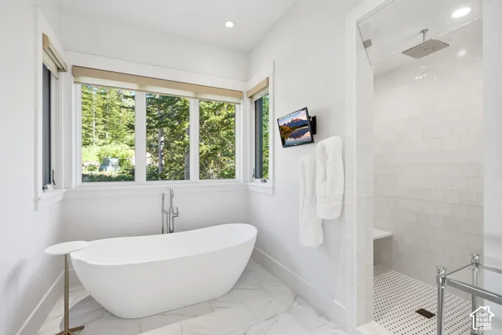 Freestanding soaking tub with chrome floor-mounted faucet, expansive window with natural scenery, and a glass-enclosed shower with a built-in bench and rain showerhead