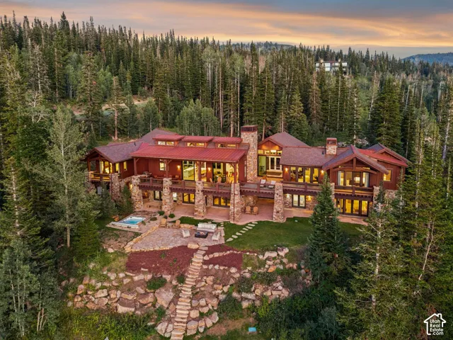 Expansive exterior featuring multi-level balconies, natural stone pillars, a built-in spa, a stone patio, and abundant mature trees