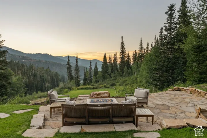 Expansive flagstone patio with a built-in fire feature, surrounded by mature evergreen trees and mountain scenery