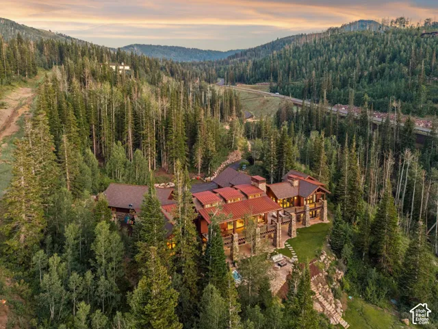Stone exterior, multiple balconies, terraced landscaping, red metal roofing, surrounding evergreen forest