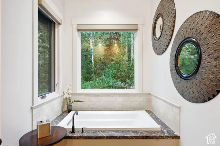 Built-in soaking tub with a dark stone-finish surround, subway tile wainscoting, and a matte black faucet