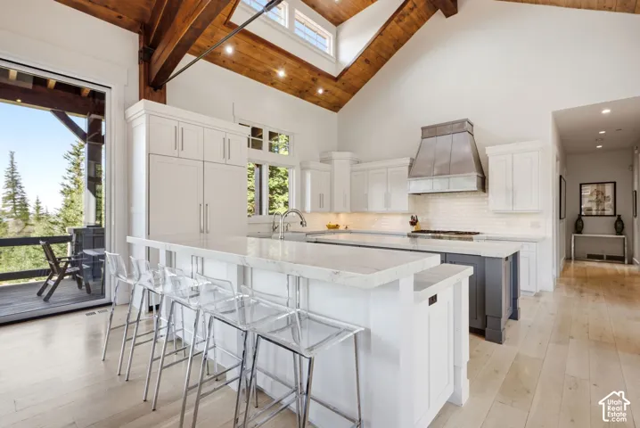 Vaulted wood-beamed ceiling, white kitchen cabinetry, double kitchen island with stone countertops, stainless steel range hood, and wood-finish flooring