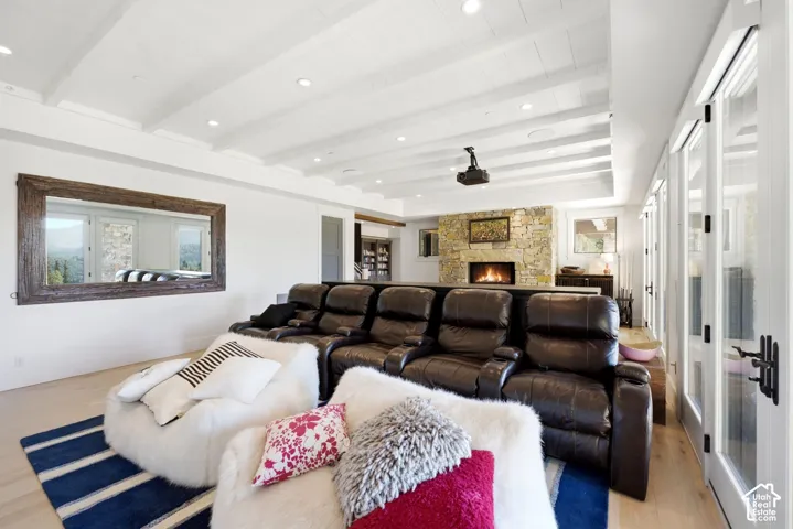 White beamed ceiling, stone fireplace with hearth, recessed lighting, light wood-finish flooring, and glass-paneled doors