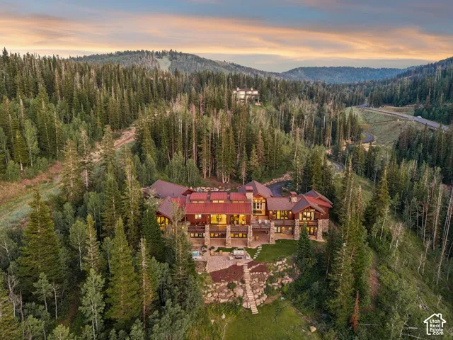 Extensive property nestled among mature evergreen trees, featuring a multi-level structure with stone and wood siding, a prominent red roof, and multiple outdoor patio spaces